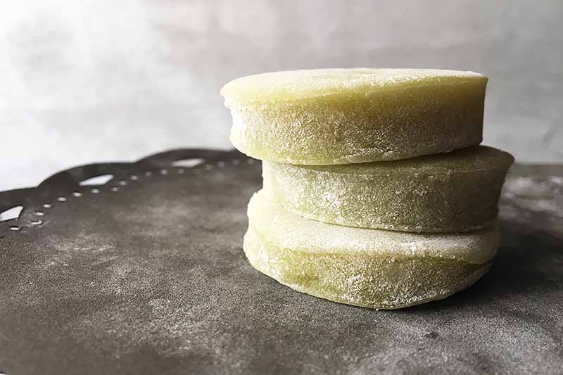 Horizontal image of a stack of three circular mochi desserts on a gray plate.
