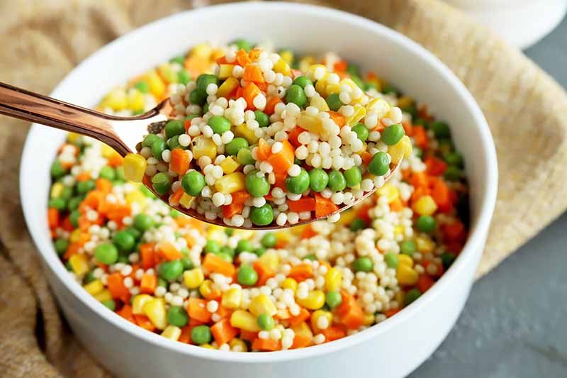 Horizontal image of a spoon holding a grain and veggie salad.