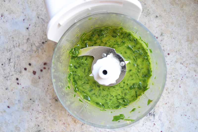 Horizontal image of a food processor with a pureed green sauce.
