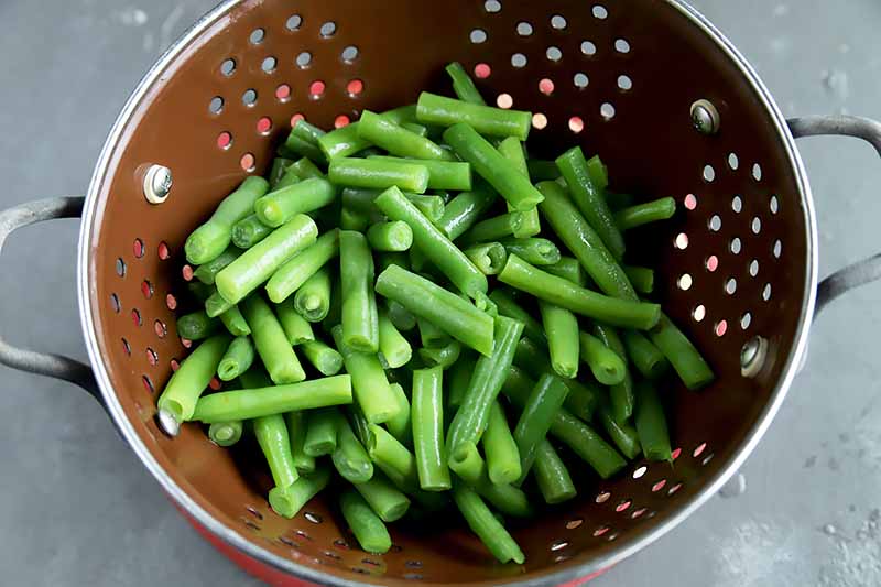 Horizontal image of a colander with blanched green beans.