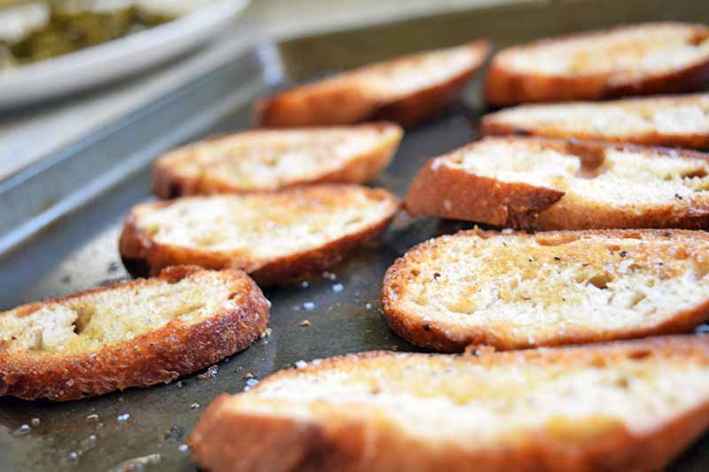 Horizontal image of toasted baguette slices on a metal baking sheet.