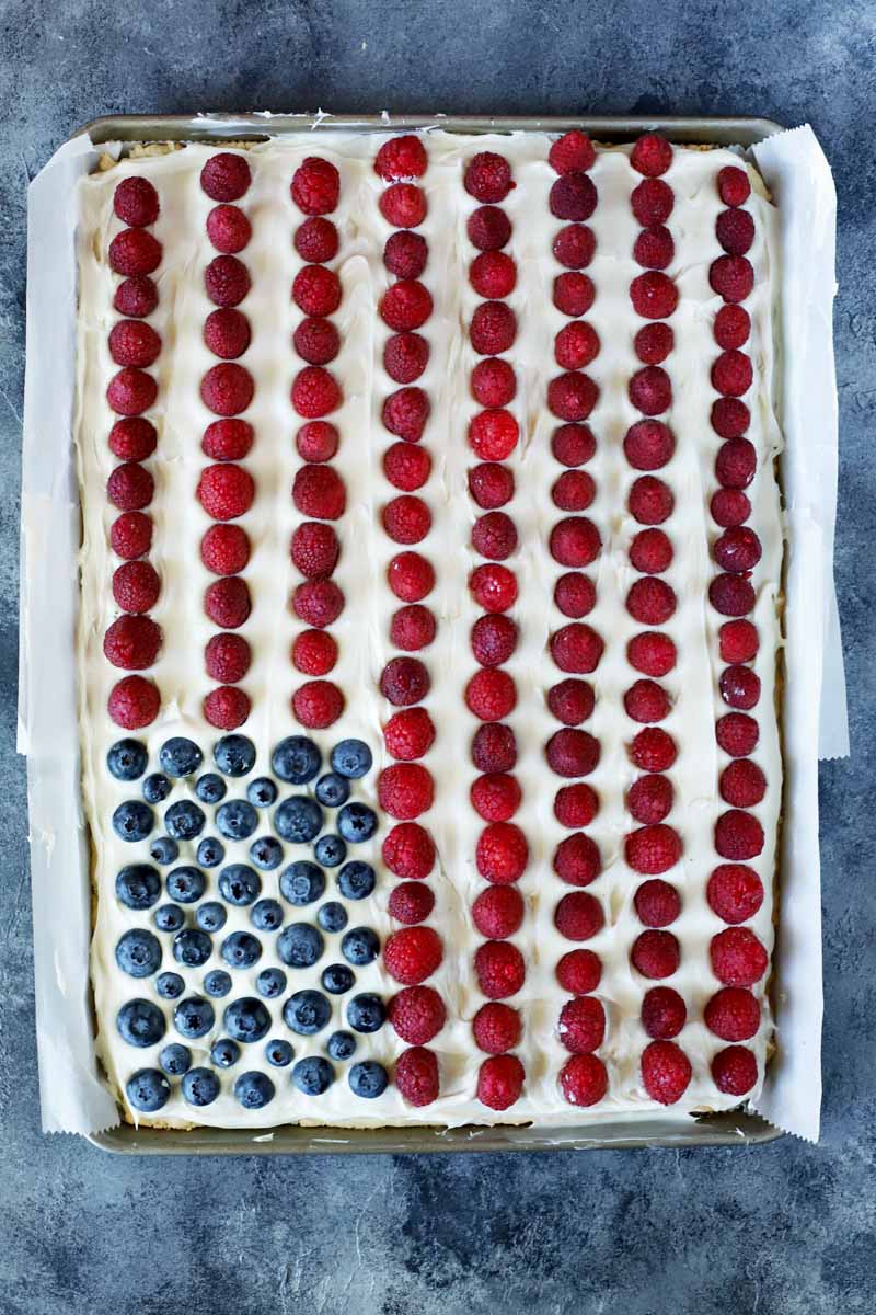 Top down view of a cookie cake made to look like an American flag with red and blue berries and white vanilla frosting.