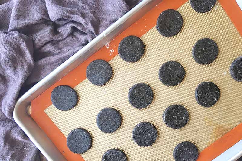 Horizontal image of a silicone mat on a sheet pan with unbaked cocoa dessert circles.