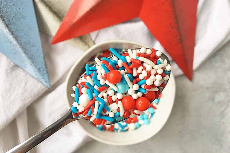Horizontal image of a spoon with assorted blue, red, and white sprinkles.