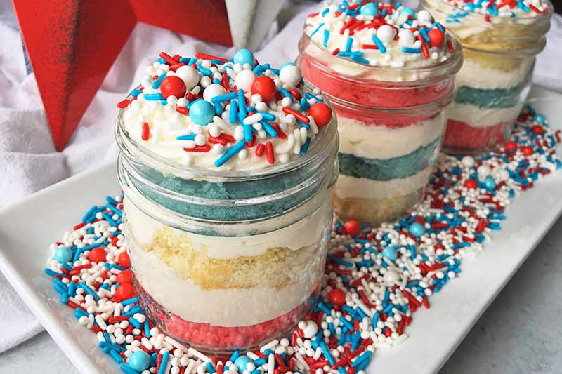 Horizontal image of three jars of trifles on a dish with bright sprinkles.