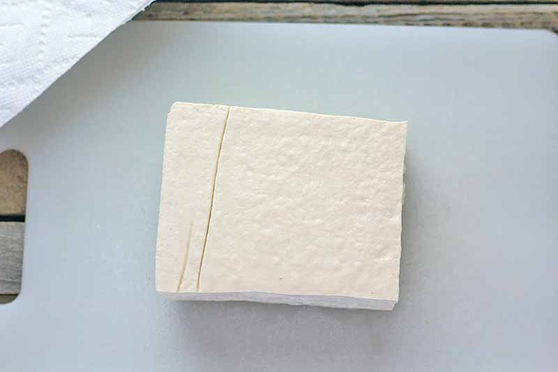 Horizontal image of a block of firm tofu on a cutting board.