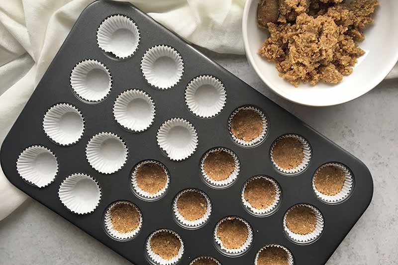 Horizontal image of a mini cupcake pan with some cups filled with a crust.