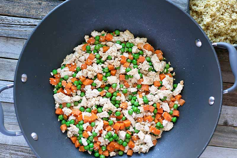 Horizontal image of a wok with tofu, carrots, and peas next to a pot with cooked quinoa.