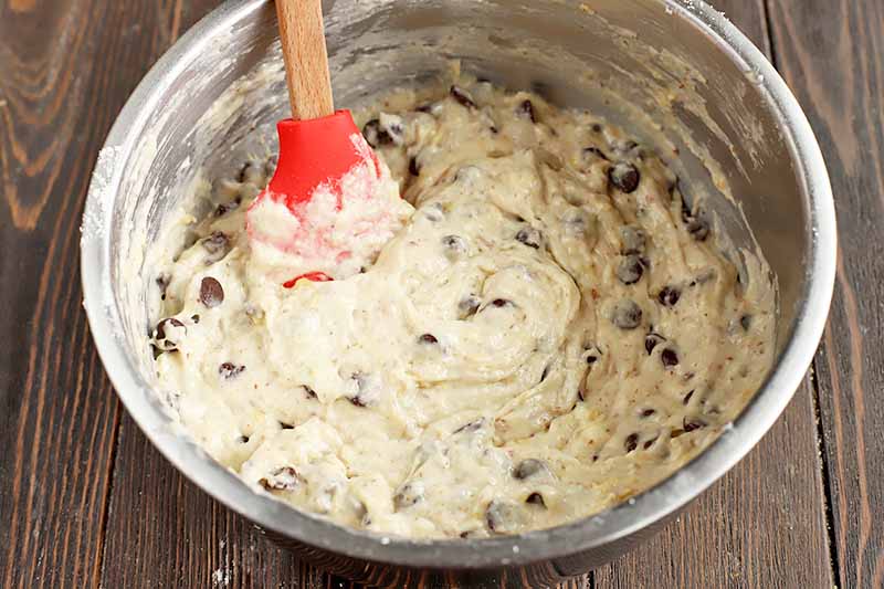 Horizontal image of a batter mixed with chocolate chips by a red spatula.