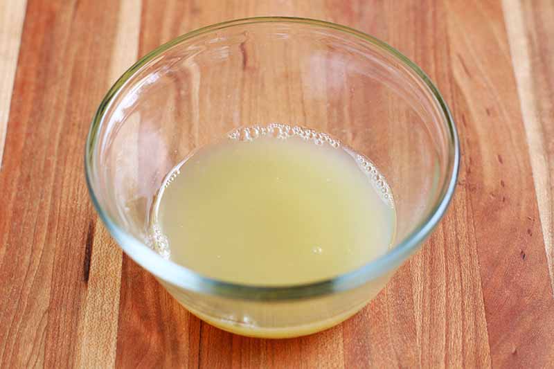 Horizontal image of a small glass bowl of honey and lemon juice, on a wood surface.