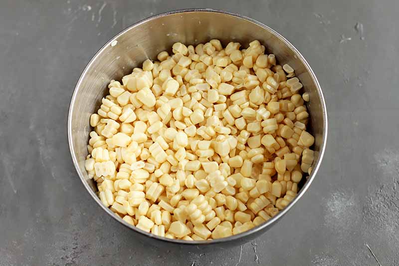 Horizontal image of fresh corn kernels in a metal bowl.