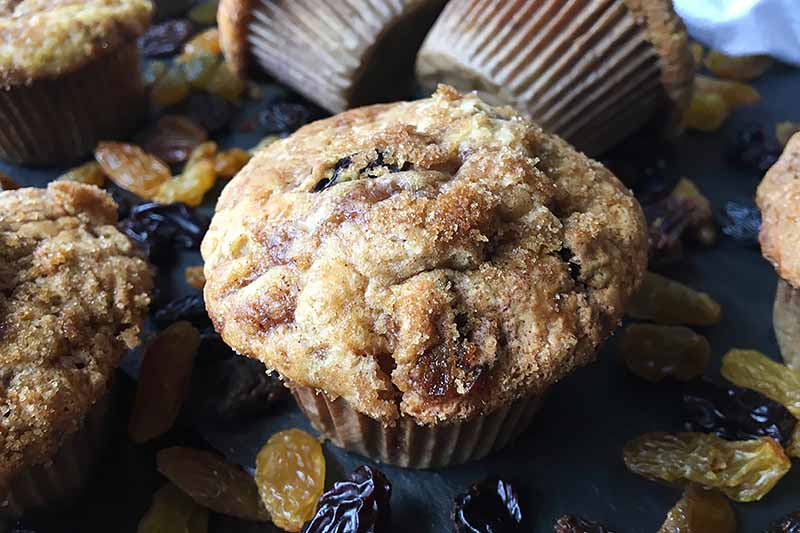Horizontal image of scattered muffins on a slate surrounded by dried fruit.