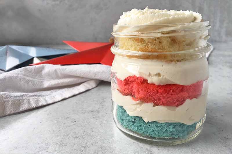 Horizontal image of a glass container with layers of colored cake and white frosting.