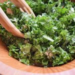 Horizontal closely cropped image of kale salad with Pecorino cheese in a large wooden salad bowl, with wooden salad tongs.