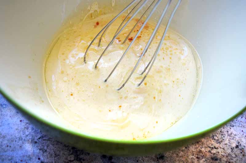 Horizontal image of whisking together eggs in a bowl.