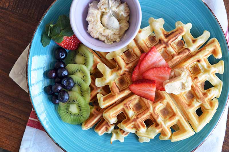 Horizontal image of a blue plate with waffles and fresh fruit.
