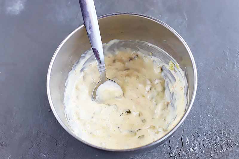 Horizontal image of a creamy white sauce with a spoon in a metal bowl.