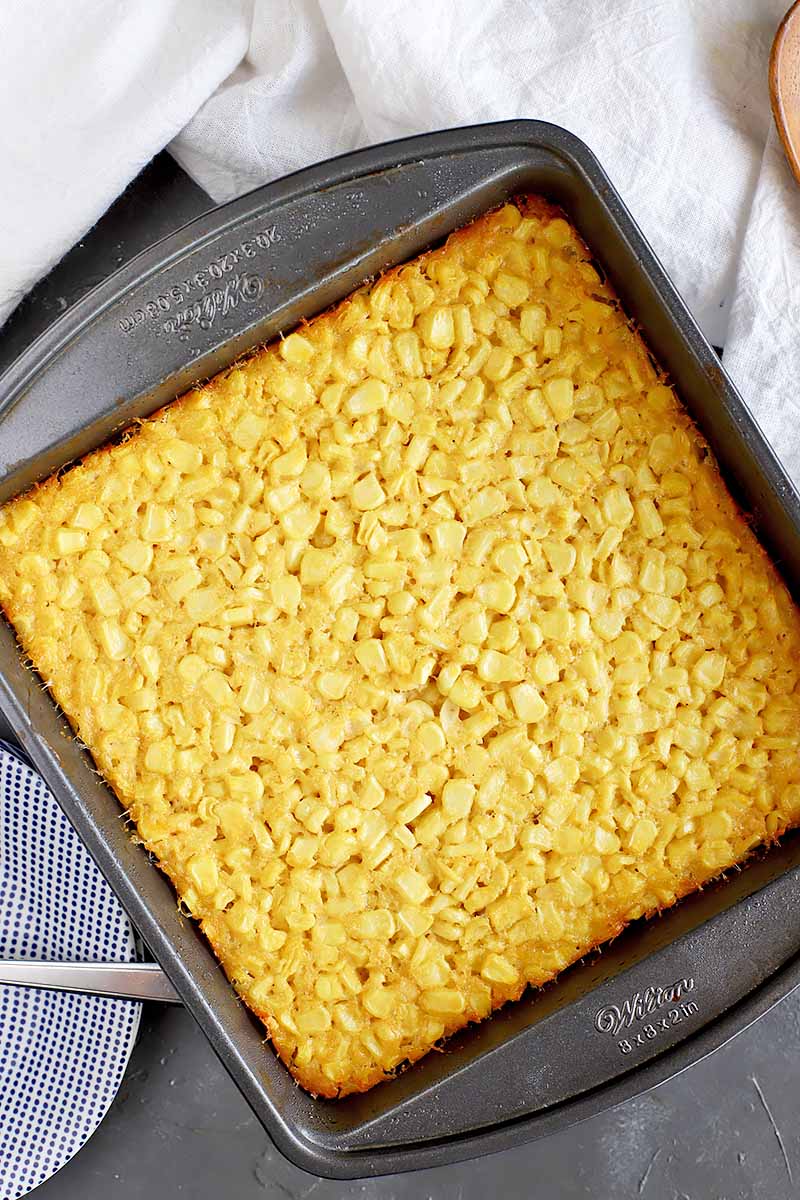 Vertical image of a square baking pan with baked corn pudding.