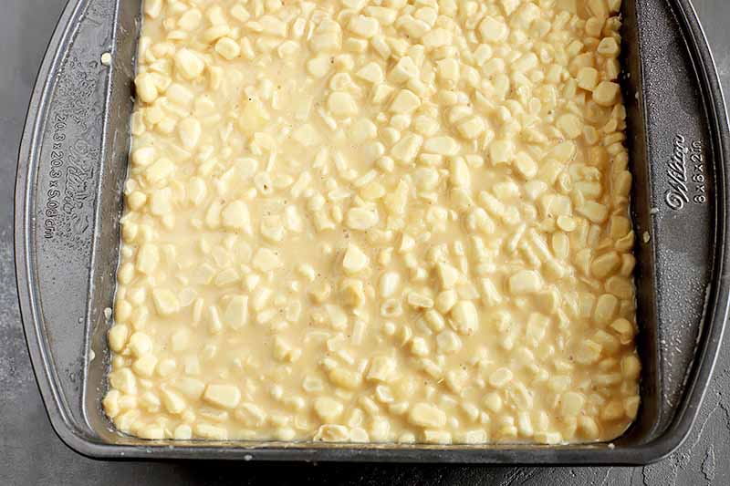 Horizontal image of an unbaked corn dish in a metal square baking pan.