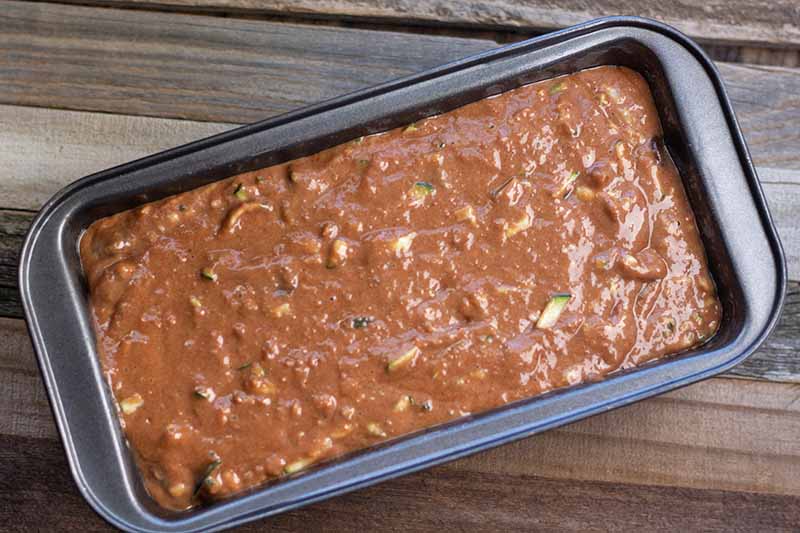 Horizontal overhead image of chocolate zucchini quick bread batter in a metal loaf pan, on a wood surface.