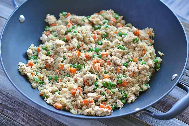 Horizontal image of a wok with a quinoa, carrot, and pea mixture.
