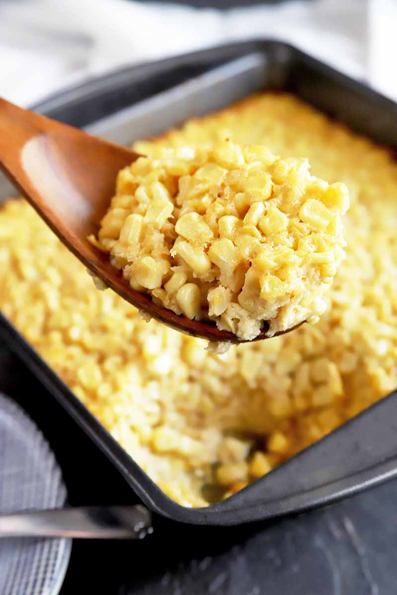 Vertical close-up image of a wooden spoon holding some corn pudding.