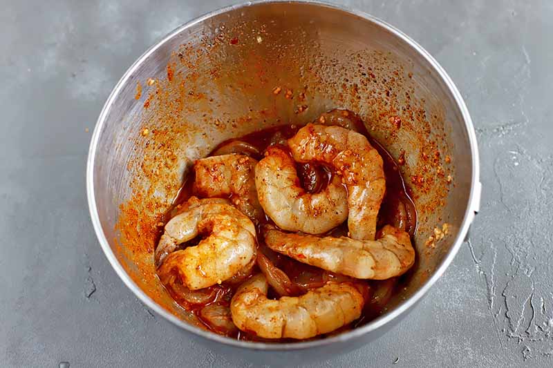 Horizontal image of seasoned and marinated shrimp in a metal bowl.