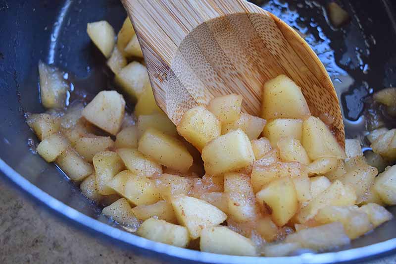 Horizontal image of a spoon mixing together apple pieces in a pot.