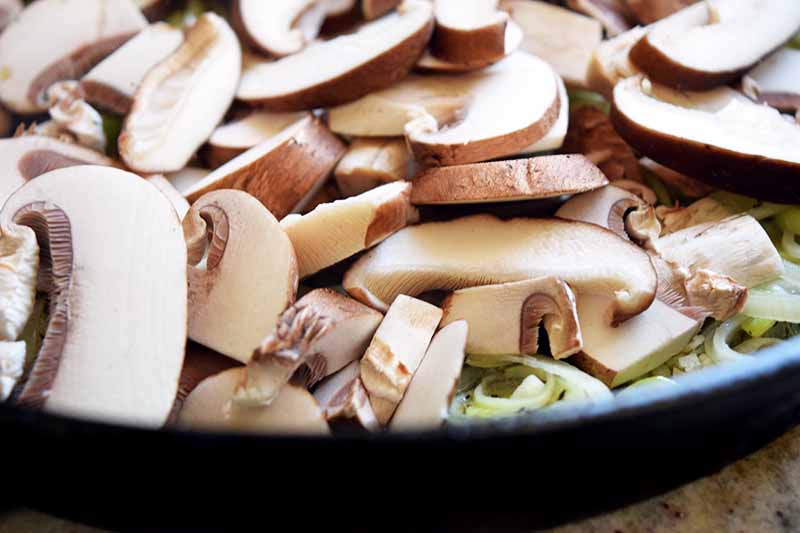 Closeup horizontal image of sliced mushrooms in a black frying pan.