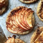 Horizontal top-down image of baked mini apple tarts with spices and granular sugar.