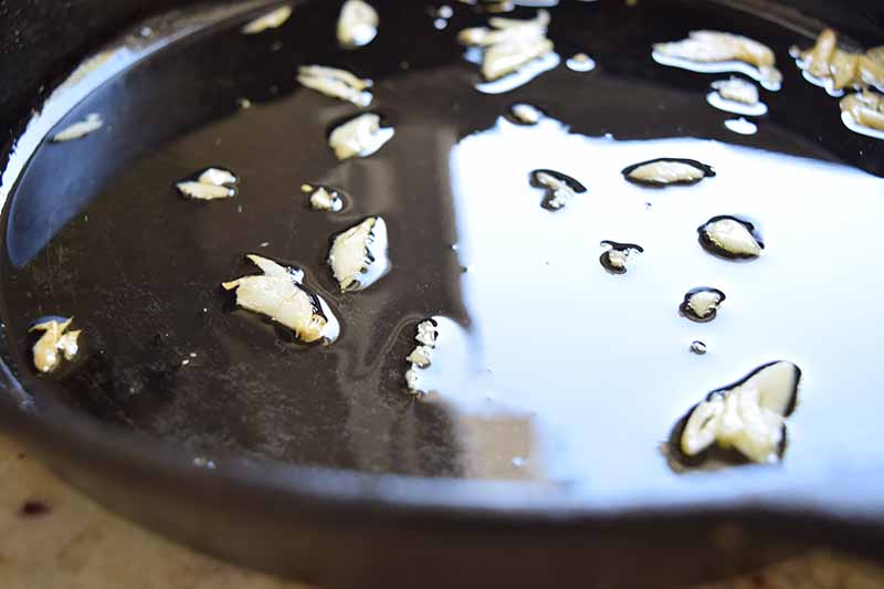 Horizontal image of oil and garlic slices in a cast iron skillet.