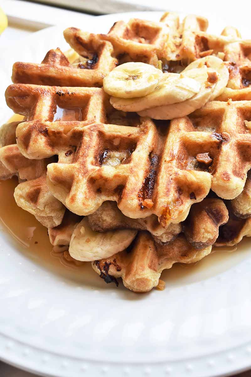 Vertical image of a white plate with a stack of fluffy waffles with syrup and slices of bananas.