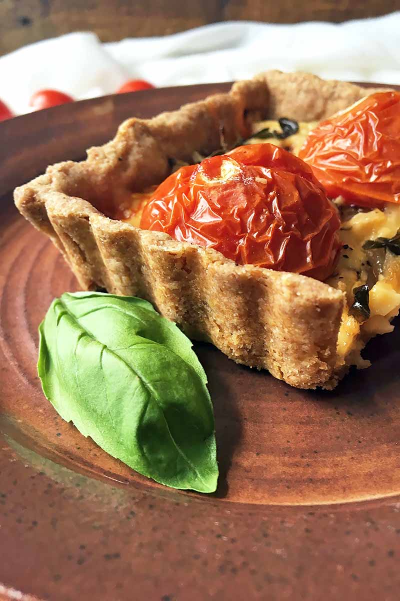 Vertical image of a basil leaf and part of a savory pastry on a brown plate.
