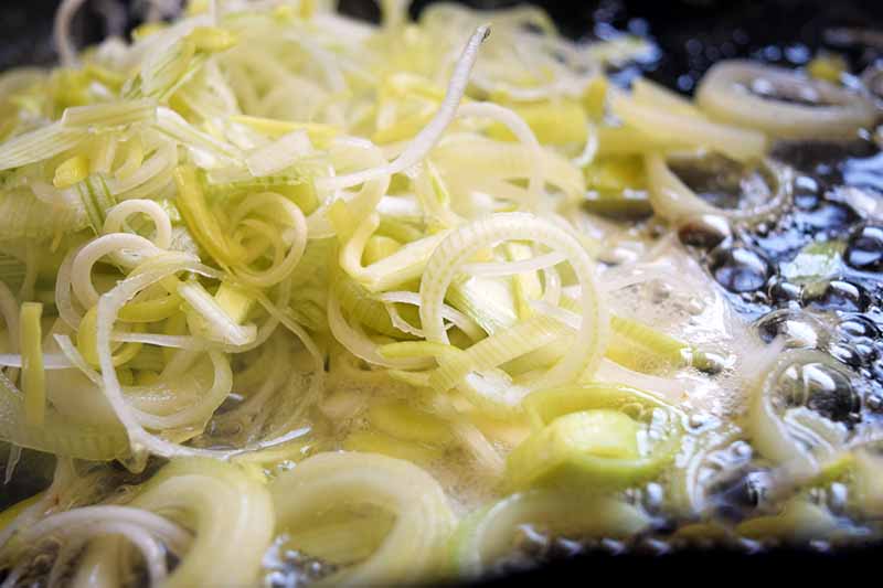Thinly sliced leeks sauteeing in a cast iron frying pan.