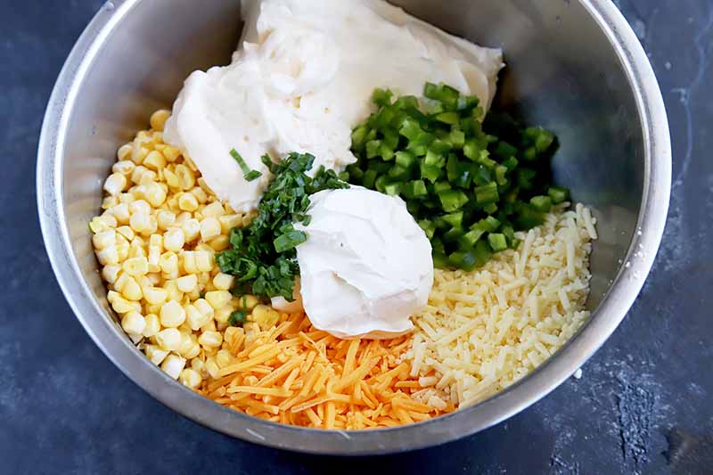 Horizontal image of white, yellow, and green ingredients unmixed in a metal bowl.