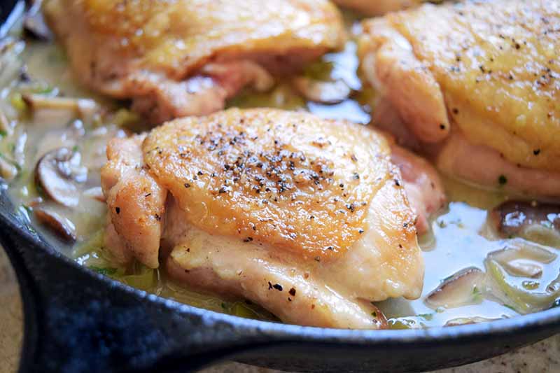 Seasoned chicken thighs with skin on, browning in a cast iron pan.