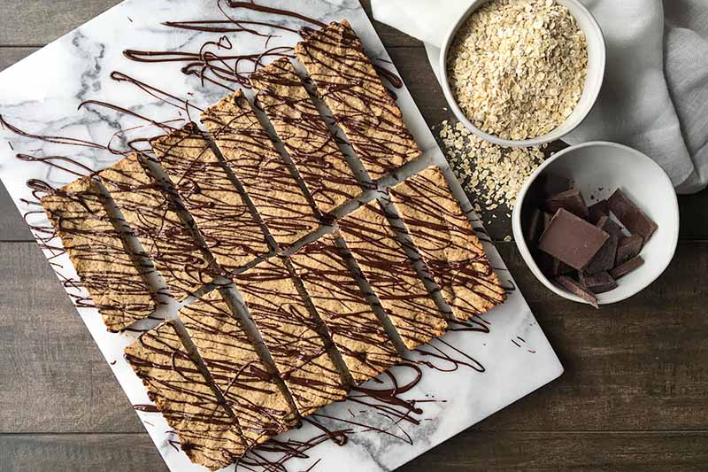 Horizontal image of a marble board with rectangular cookies drizzled with chocolate.