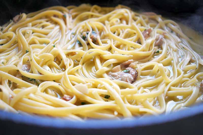 Horizontal head-on image of cooked pasta with clams in liquid in a large frying pan.
