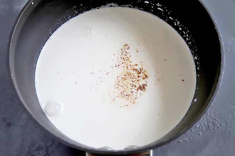 Horizontal image of a saucepan with cream and flavorings.