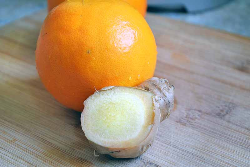 Horizontal image of an orange and a knob of ginger on a wooden cutting board.