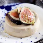 Horizontal image of a creamy dessert garnished with three sliced figs and honey on a blue and white plate.