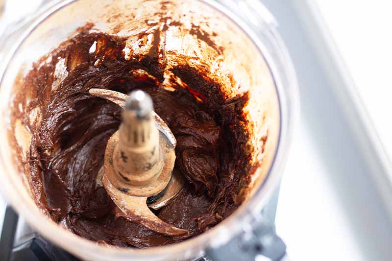 Horizontal image of a food processor with a thick chocolate mixture.