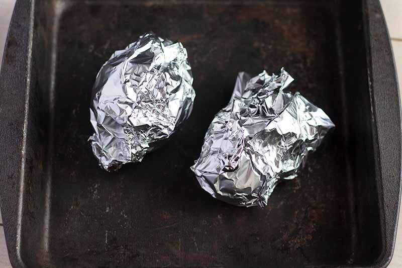 Horizontal overhead image of a metal rimmed sheet pan with two beets wrapped in aluminum foil at the center.