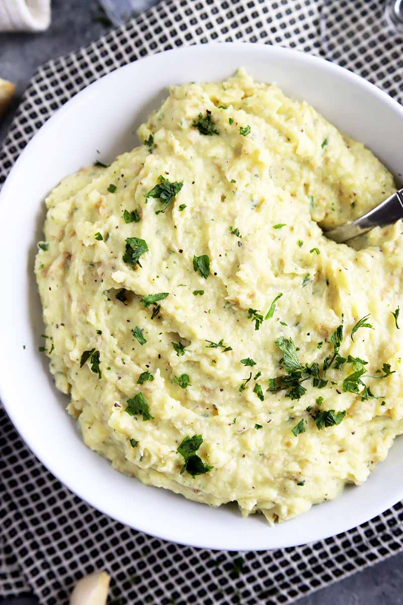Vertical top-down image of a white dish of mashed potatoes with parsley.