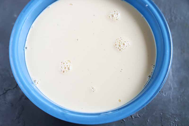 Horizontal image of a blue bowl filled with a creamy white mixture on a black surface.