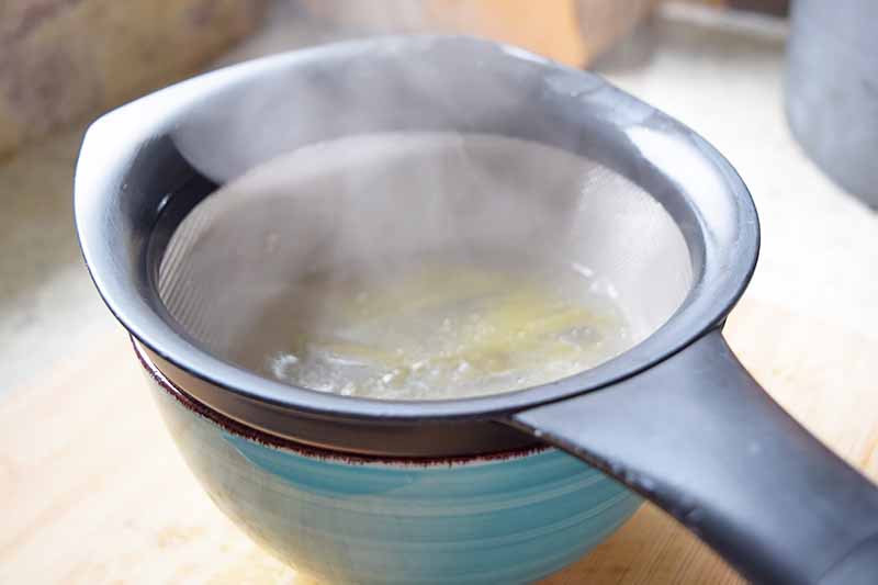 Horizontal image of straining a yellow liquid in a blue bowl.