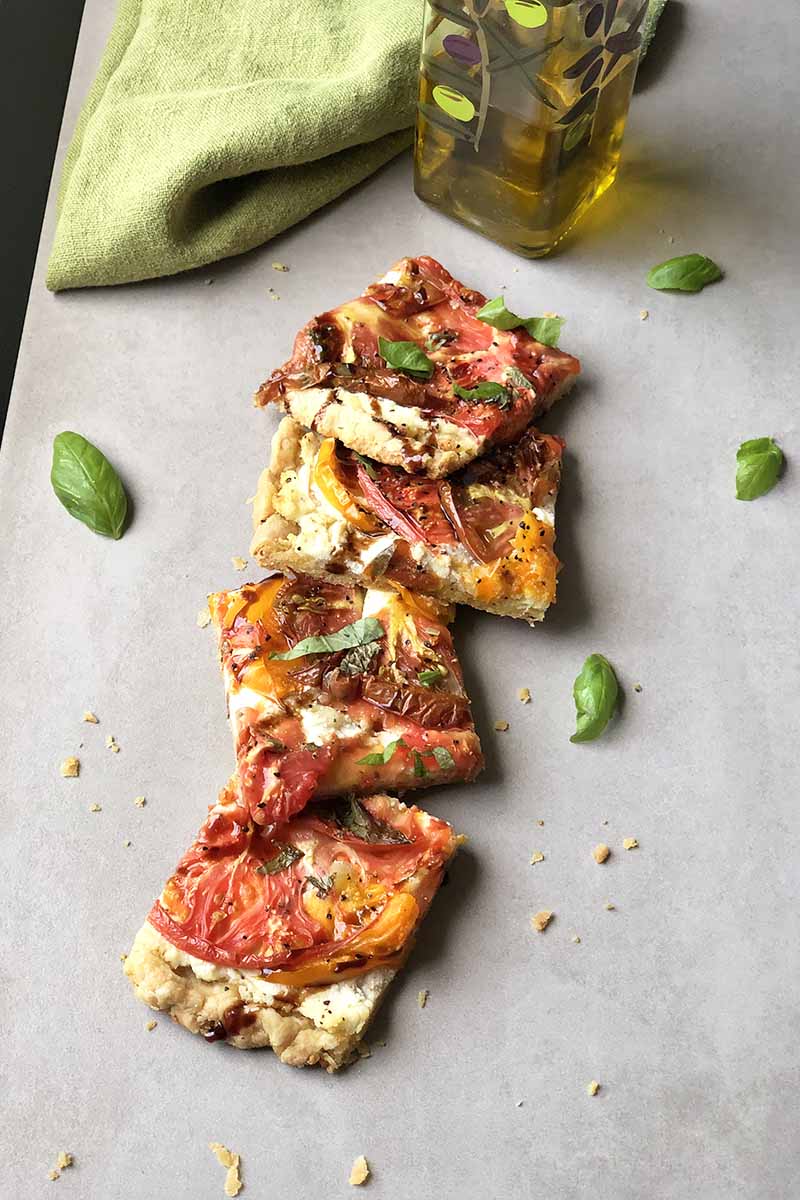 Vertical image of shingled square slices of pizza next to fresh basil.