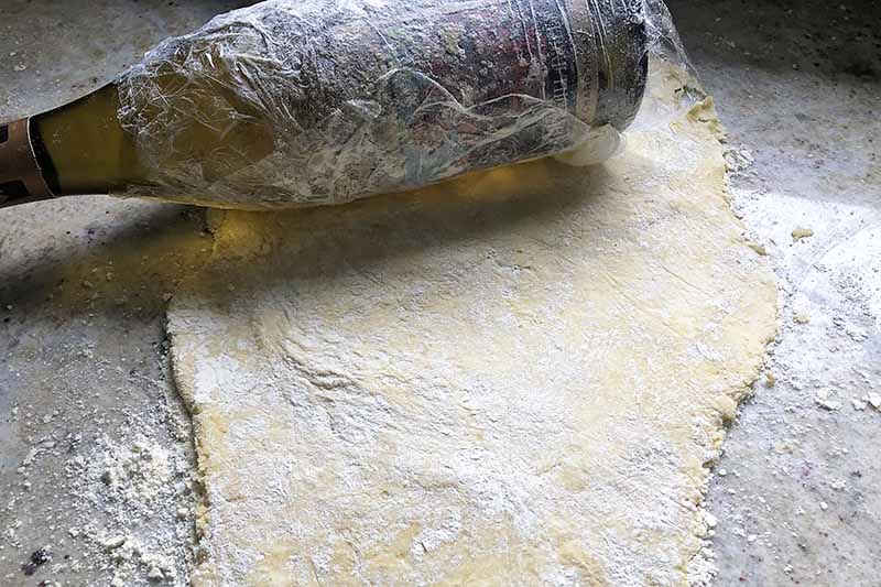 Horizontal image of a wine bottle rolling out a lightly floured dough.