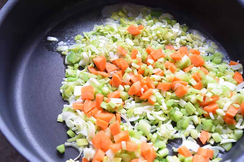 Horizontal image of cooking chopped onions, carrots, and celery.