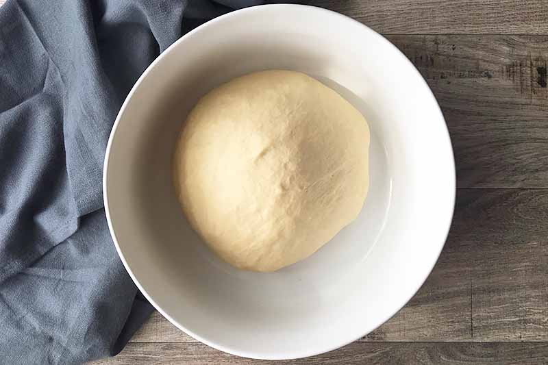 Horizontal image of a fermented round of dough in a white bowl.